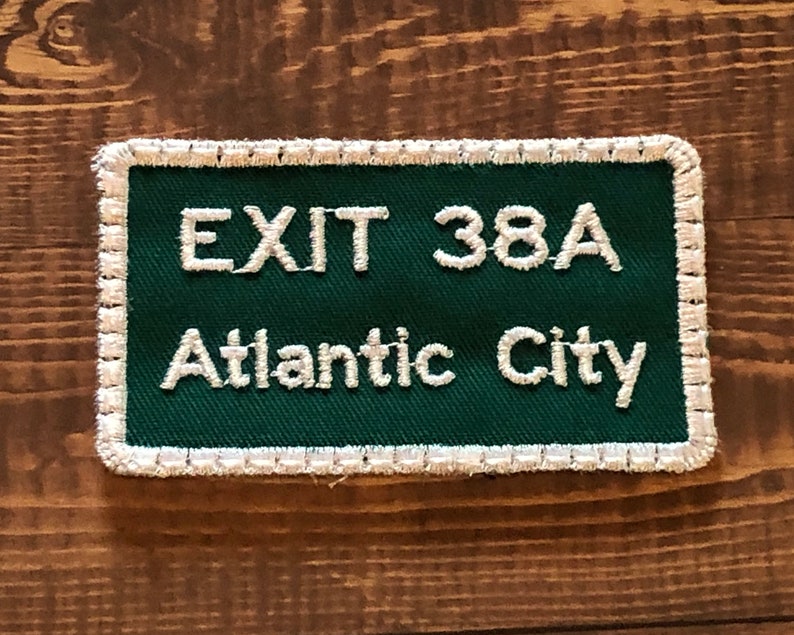 Puede incluir: Parche bordado verde y blanco con costuras blancas alrededor de los bordes. El parche dice "EXIT 38A Atlantic City".