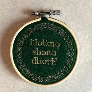 May include: A green felt hoop with a gold embroidered Celtic knot border and the text "Nollaig shona duit!" in gold thread.
