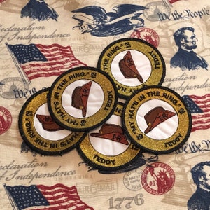 May include: Five gold and white embroidered patches with the text "My Hat's In The Ring '12" and "Teddy" around a white circle with a brown hat and the letters "TR" inside.