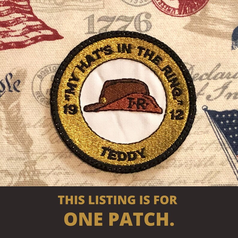 May include: A gold and black embroidered patch with a brown hat and the text "My Hat's In The Ring 1912 Teddy"