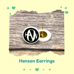 May include: White and black round stud earrings with the letters "AN" in a bold, stylized font. The earrings have a gold-colored post and are labeled "Hanson Earrings".