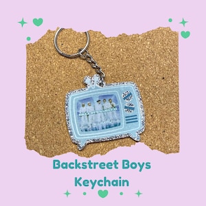 Puede incluir: Un llavero azul claro con forma de televisor retro, con una foto de los Backstreet Boys. El llavero tiene un borde plateado brillante y un llavero plateado. El texto "Backstreet Boys Keychain" está debajo.