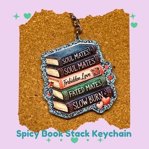 Peut inclure: Un porte-clés représentant une pile de cinq livres avec des titres tels que "Soul Mates" et "Forbidden Love". Le porte-clés a une bordure scintillante et des cœurs décoratifs. Le texte "Spicy Book Stack Keychain" est en bas.