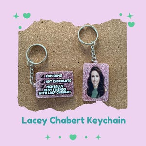 May include: Two pink glitter keychains. One keychain has a photo of a woman, the other has text that reads "ROM COMS, HOT CHOCOLATE, MENTALLY BEST FRIENDS WITH LACY CHABERT". The text "Lacey Chabert Keychain" is at the bottom.