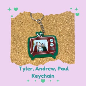 May include: A keychain featuring a red and green television design with a family photo inside. The keychain has a silver chain and ring. The text "Tyler, Andrew, Paul Keychain" is below the keychain.