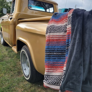 May include: A vintage gold pickup truck with a red, white, and blue striped blanket and a dark blue blanket hanging from the back.