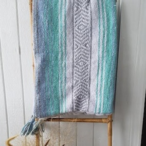 May include: A blue and white striped throw blanket draped over a wooden ladder. The blanket has a woven pattern with a diamond design. The ladder is made of natural bamboo.