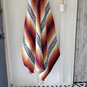 May include: A colorful striped throw blanket with red, yellow, black, and white stripes. The blanket is made of a soft, woven fabric and has a fringed edge.