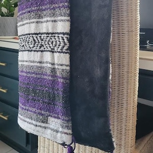 May include: A purple and white striped throw blanket with black accents and tassels. The blanket is draped over a wicker chair.