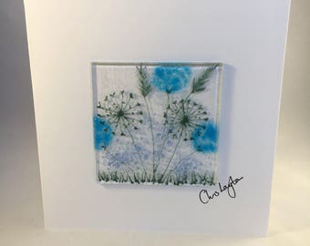 May include: A white card featuring a blue and green glass artwork of flowers. The artwork is signed "Chris Layton".