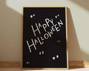 May include: A framed black poster with the words "Happy Halloween" in white, along with several white eye illustrations. The frame is a light brown color, and the poster is leaning against a wall.