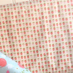 May include: A close-up of a cream-colored fabric with a repeating pattern of pink and red strawberries. The fabric is folded in half and the Riley Blake Designs logo is visible in the corner.