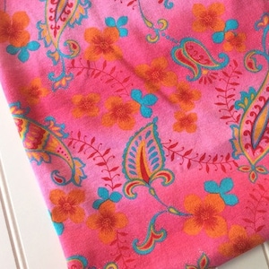 Peut inclure: Tissu rose avec un motif paisley et floral. Le tissu pr&eacute;sente un d&eacute;grad&eacute; de nuances de rose, avec un rose plus fonc&eacute; en haut et un rose plus clair en bas. Les motifs paisley et floraux sont dans des tons d'orange, de jaune, de bleu et de rouge.