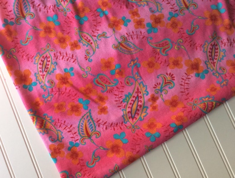 Peut inclure: Tissu rose avec un motif paisley et floral dans des tons d'orange, bleu et rouge.