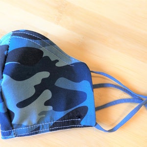 May include: Blue camouflage face mask with adjustable ear loops. The mask is made of a soft, breathable fabric and has a comfortable fit.