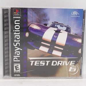 May include: A PlayStation game case for "Test Drive 6." The cover features a purple sports car with white stripes, set against a blurred background. The game's title and the number 6 are prominently displayed. The case includes the PlayStation logo and the ESRB rating.