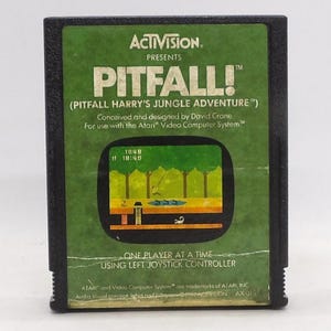 May include: A vintage Atari Pitfall! video game cartridge. The green label features the game's title, a jungle scene, and the Activision logo. The cartridge is black and includes the text "ONE PLAYER AT A TIME USING LEFT JOYSTICK CONTROLLER."