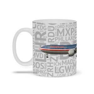May include: White ceramic mug with a gray and white design featuring a plane with the words "American" on the side. The design also includes a variety of airport codes, such as ORD, LAX, and JFK.