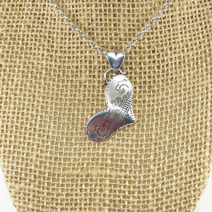 May include: A silver necklace with a heart-shaped pendant. The pendant has a detailed design of swirls and lines.