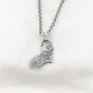 May include: A silver necklace with a detailed heart pendant. The heart is intricately designed with swirls and lines.