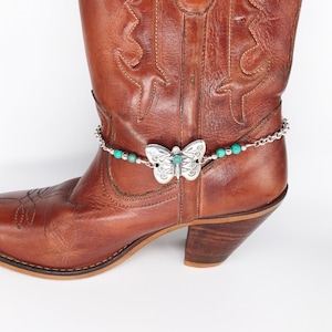 May include: Brown leather cowboy boot with a silver butterfly charm and turquoise beads on a chain ankle bracelet.