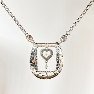 Pode incluir: Um colar de prata com um pingente em forma de cora&ccedil;&atilde;o. O pingente tem uma pequena p&eacute;rola no centro e &eacute; rodeado por um design delicado. O colar &eacute; feito de uma corrente com pequenas contas de prata.