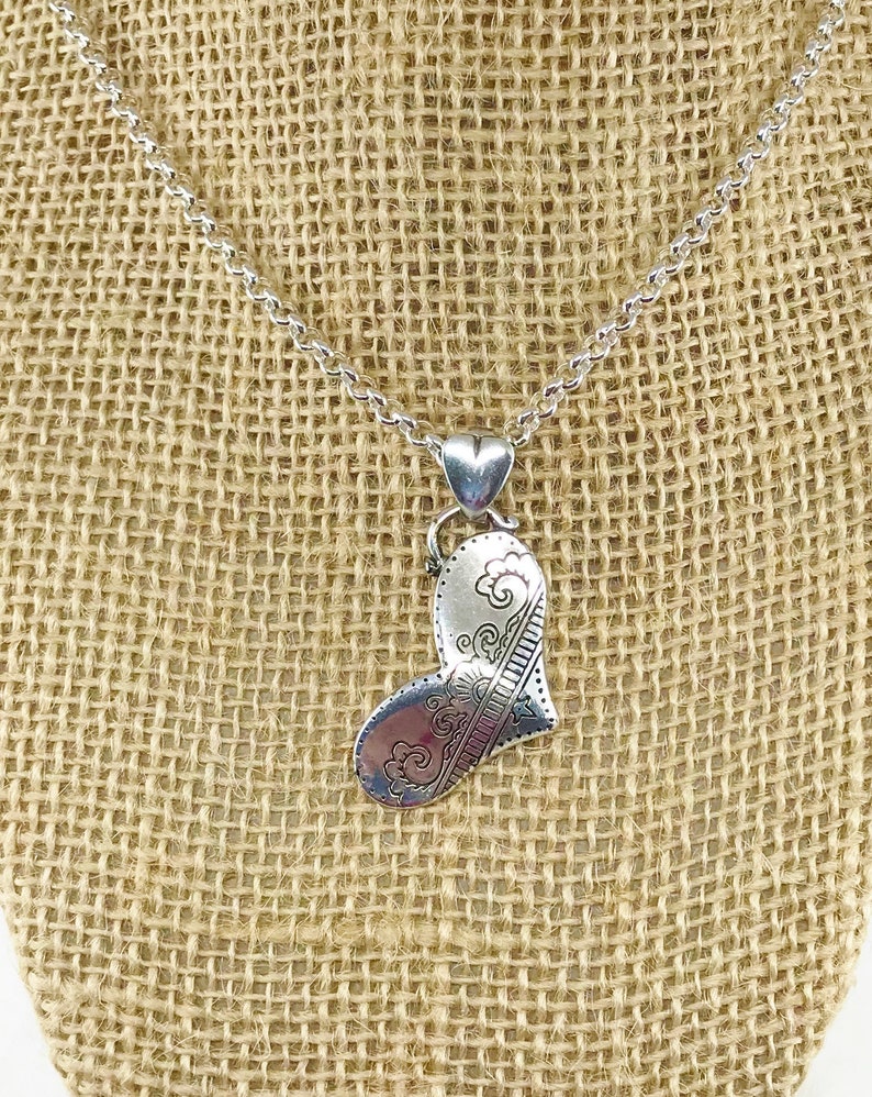 May include: A silver necklace with a heart-shaped pendant. The pendant has a detailed design of swirls and lines.