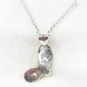 May include: A silver necklace with a heart-shaped pendant. The pendant has an intricate design of swirls and lines.