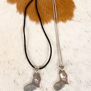 May include: Two silver heart necklaces with intricate designs. One necklace has a black cord and the other has a silver chain.