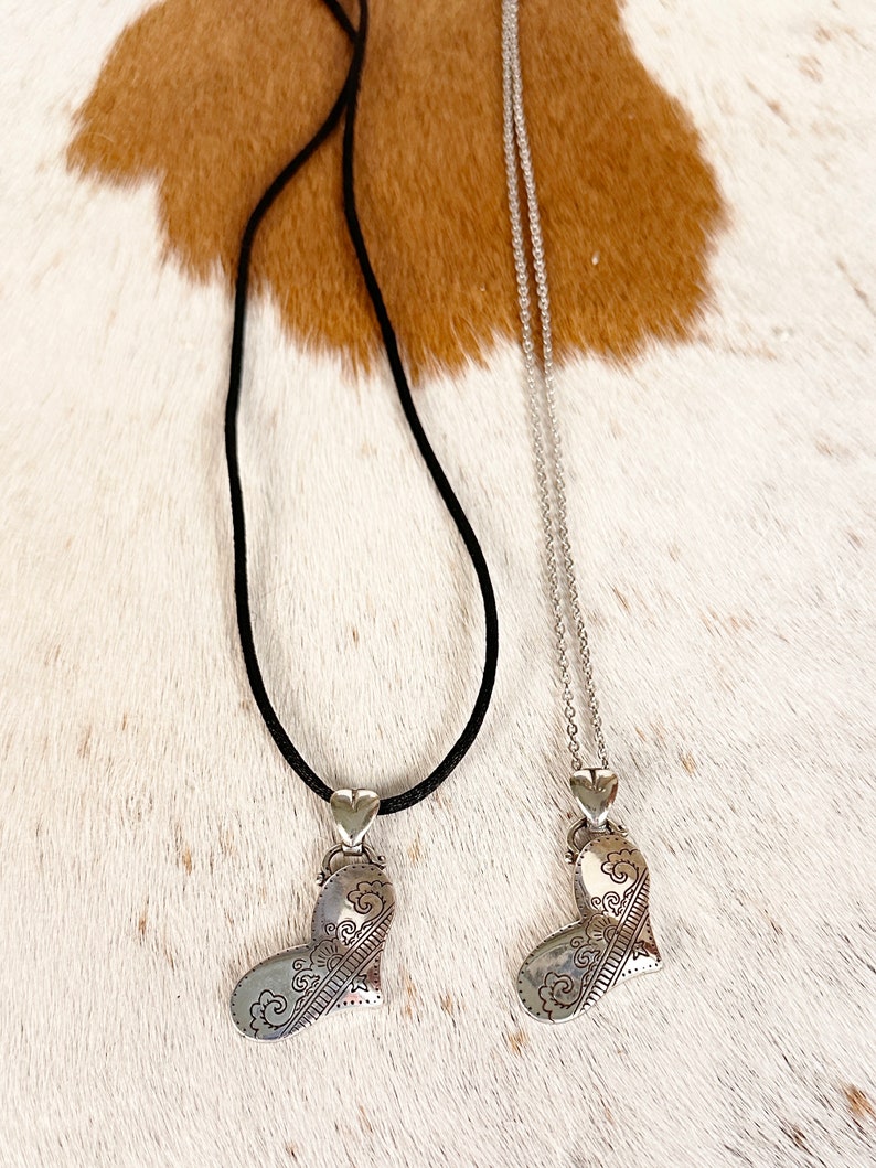 May include: Two silver heart necklaces with intricate designs. One necklace has a black cord and the other has a silver chain.