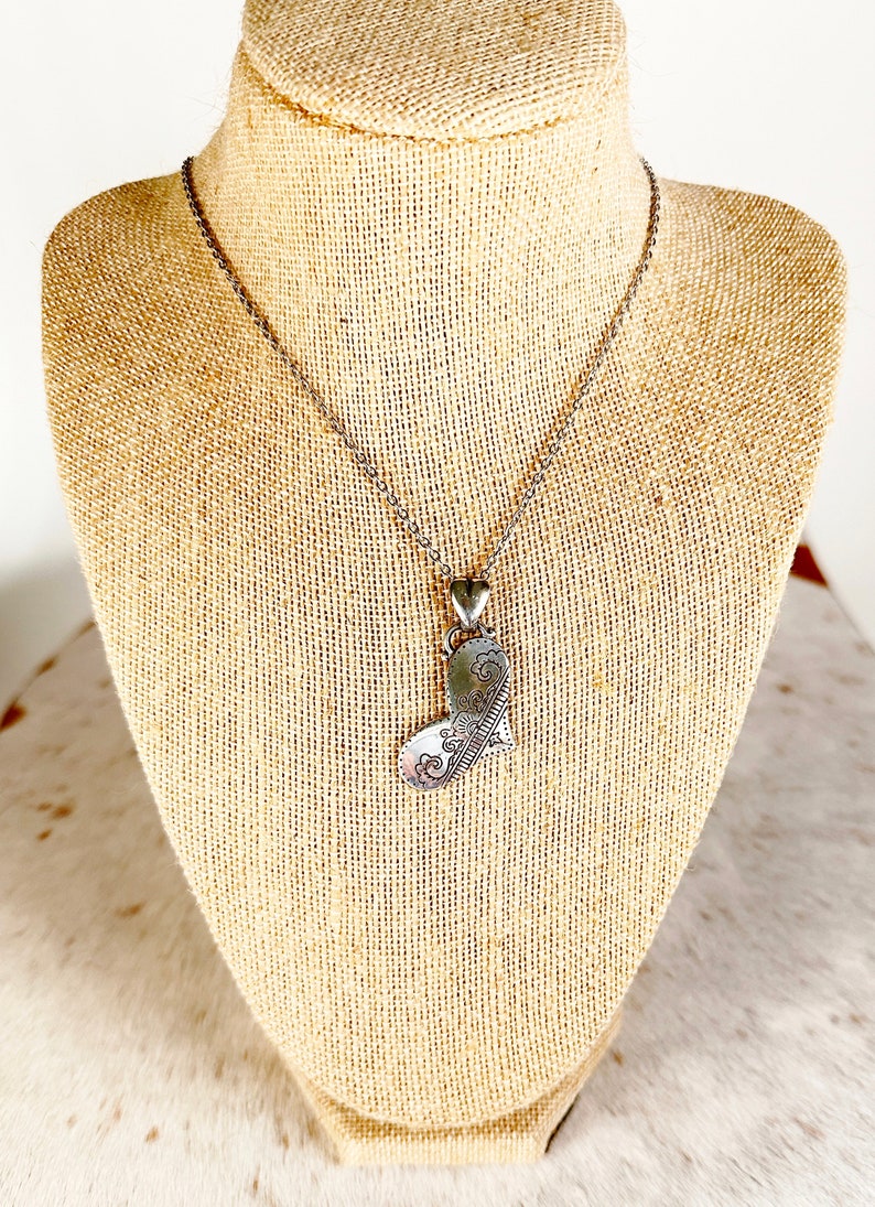 May include: A silver necklace with a detailed heart pendant. The heart is intricately designed with a floral pattern.