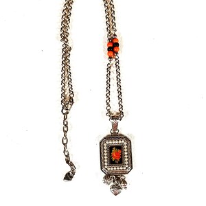 May include: Silver necklace with a rectangular pendant. The pendant has a red rose design on a black background, framed by faux pearls. The chain includes orange and black beads and heart charms.