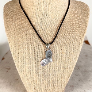 May include: A silver heart-shaped pendant necklace with intricate floral designs, hanging from a black cord on a mannequin.