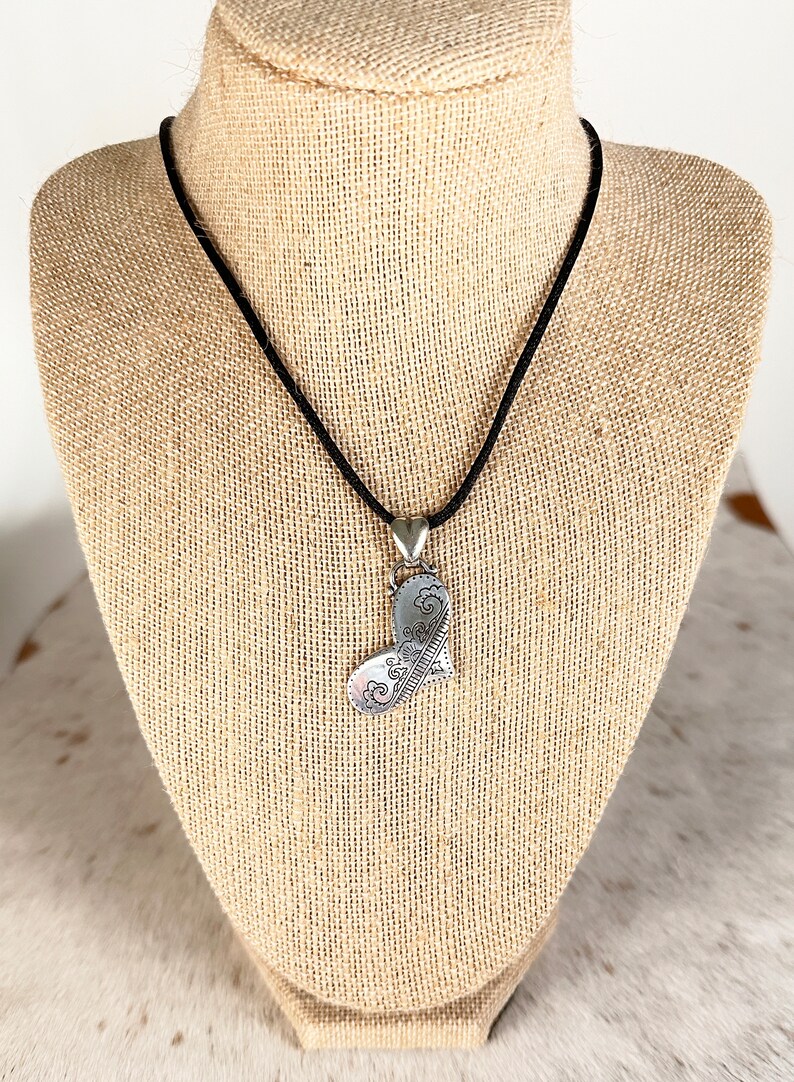May include: A silver heart-shaped pendant necklace with intricate floral designs, hanging from a black cord on a mannequin.