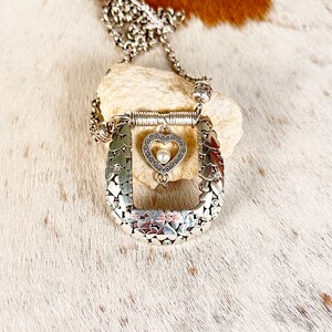 Pode incluir: Colar de prata com um pingente em forma de cora&ccedil;&atilde;o e um amuleto em forma de ferradura. A ferradura &eacute; feita de muitos cora&ccedil;&otilde;es pequenos.