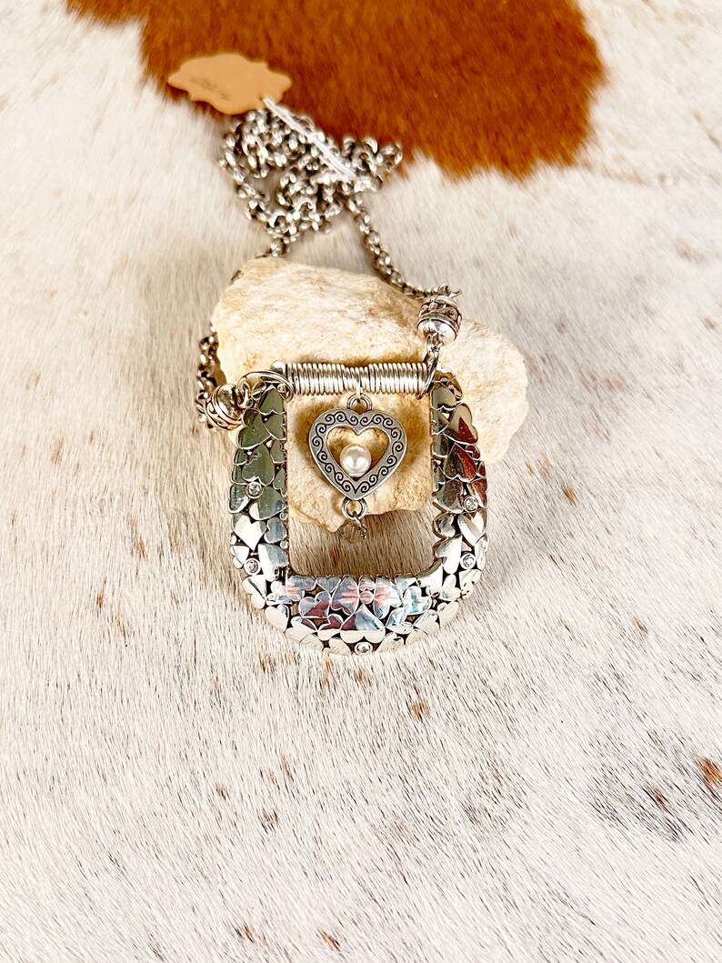 Pode incluir: Colar de prata com um pingente em forma de cora&ccedil;&atilde;o e um amuleto em forma de ferradura. A ferradura &eacute; feita de muitos cora&ccedil;&otilde;es pequenos.