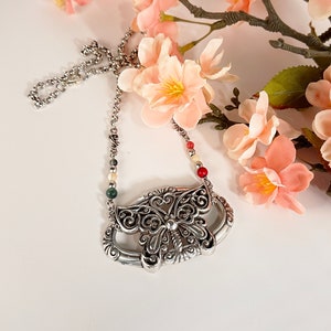 May include: A silver butterfly pendant necklace with a delicate chain and colorful beads. The butterfly has intricate details and a filigree design.