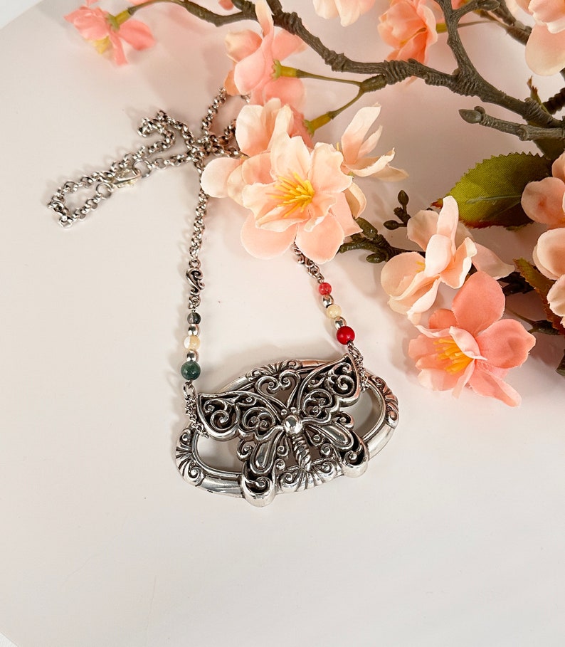 May include: A silver butterfly pendant necklace with a delicate chain and colorful beads. The butterfly has intricate details and a filigree design.