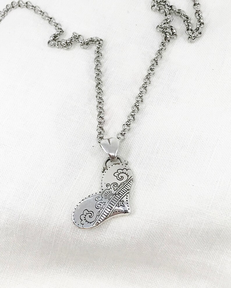 May include: A silver necklace with a detailed heart pendant. The heart is intricately designed with swirls and lines.