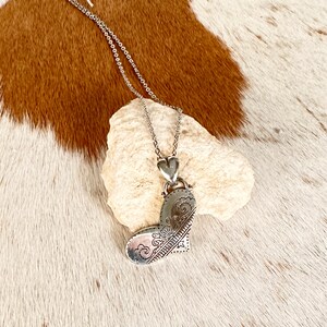 May include: A silver necklace with a heart-shaped pendant. The pendant has a detailed design of swirls and lines.