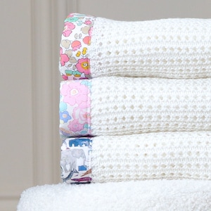 May include: A stack of four white crocheted baby blankets with colorful floral and animal print trim.