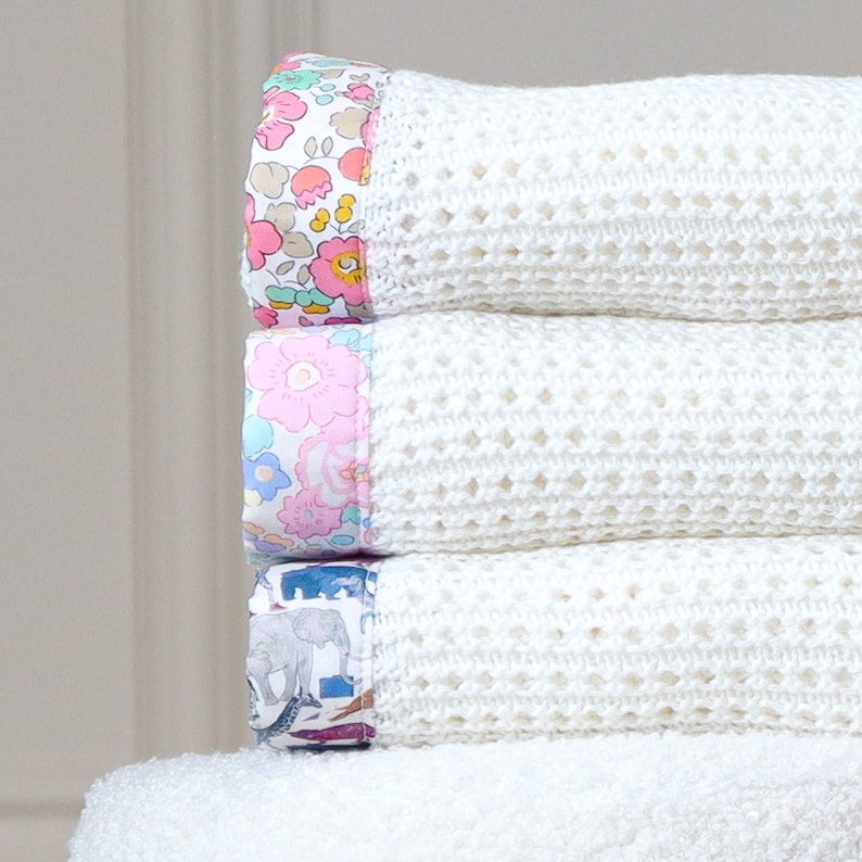May include: A stack of four white crocheted baby blankets with colorful floral and animal print trim.
