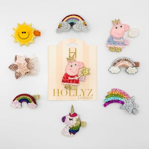 May include: A set of 9 glitter hair clips featuring a rainbow, a star, a sun, a unicorn, and a pig wearing a crown. The clips are packaged on a card with the text "Hollyz London".