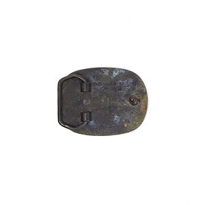 May include: Vintage oval belt buckle with a dark bronze finish. The buckle has a rectangular bar and two loops for the belt. The back of the buckle has engraved text. The buckle is likely made of metal.