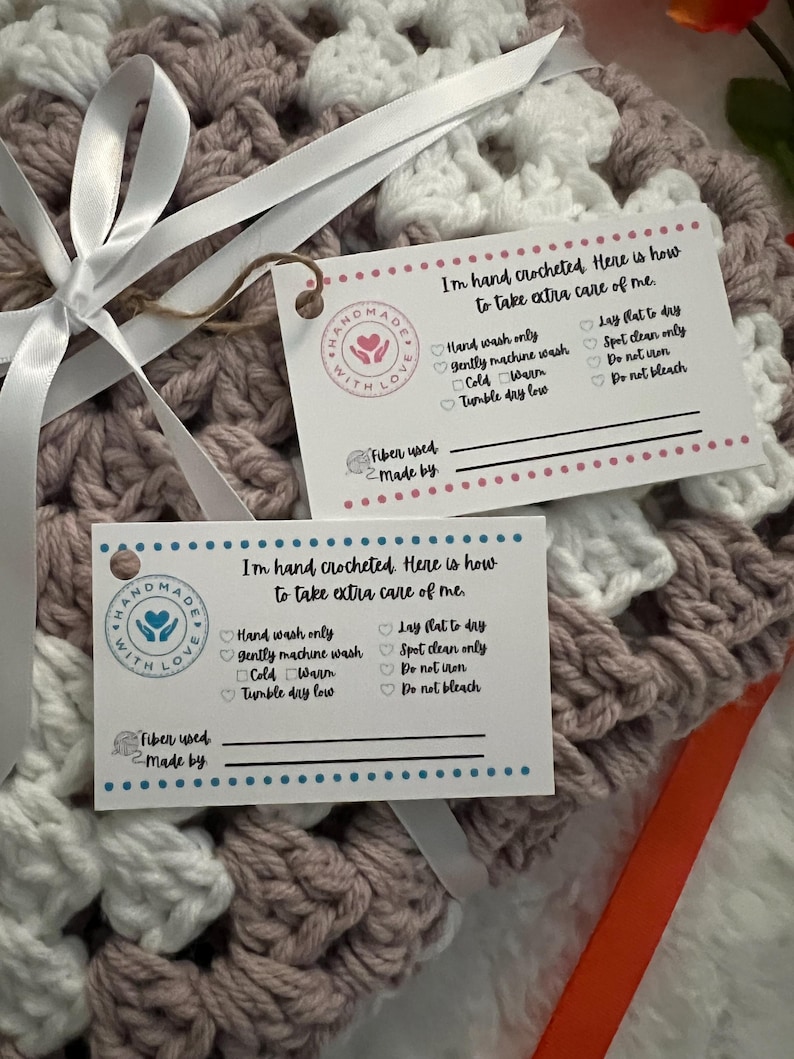 May include: A pink and white crocheted blanket with a care tag attached. The tag says "I'm hand crocheted. Here is how to take extra care of me." and lists instructions for washing and drying the blanket. The tag also has a space to write in the fiber used and who made the blanket.