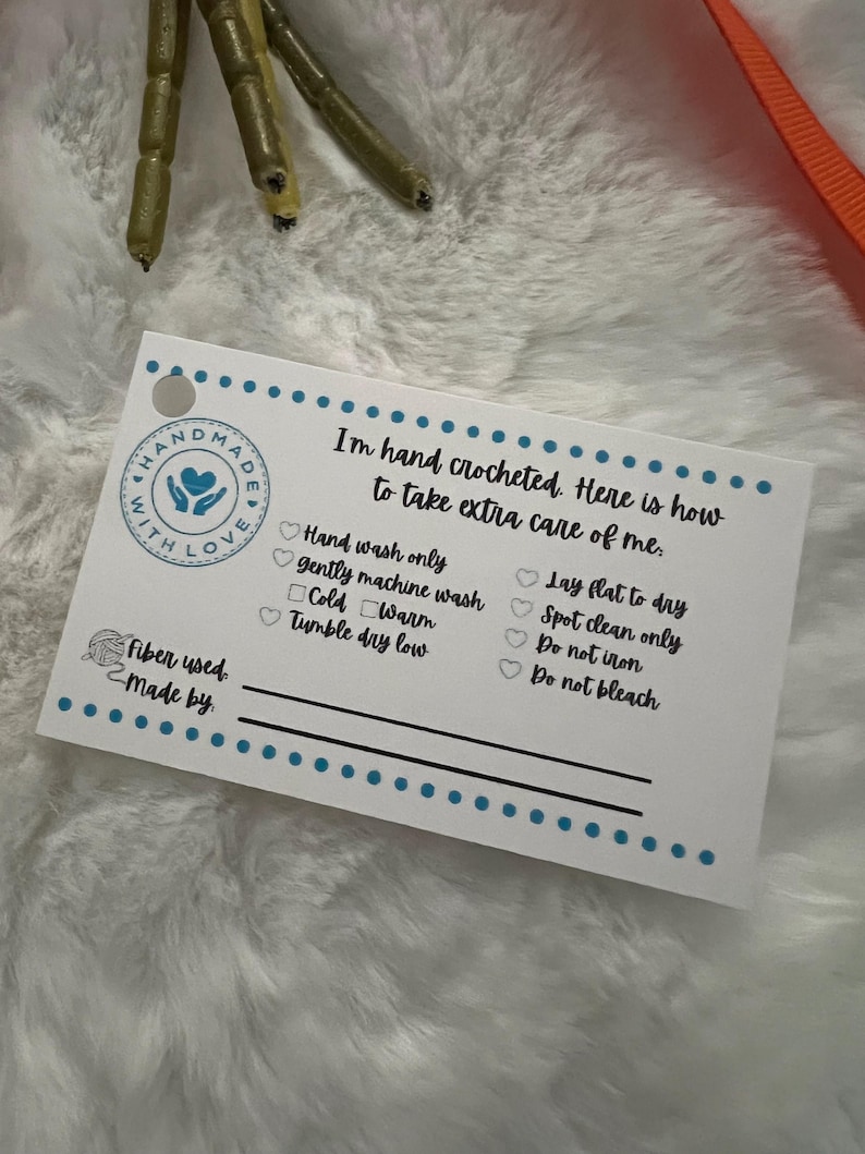 May include: White card with blue and black text and a heart logo that says "Handmade with Love". The card lists care instructions for a crocheted item, including hand washing, gentle machine washing, tumble drying low, laying flat to dry, spot cleaning, and not ironing or bleaching.
