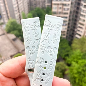 May include: Two light blue silicone watch straps with embossed Disney character faces. The characters include Mickey Mouse, Minnie Mouse, Donald Duck, and Goofy.