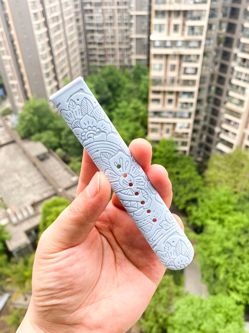 May include: A light blue watch band with a white floral pattern.