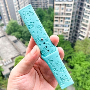 May include: A light blue silicone watch band with a variety of embossed cartoon characters, including Mickey Mouse, ghosts, and pumpkins. The band is designed for a smartwatch.