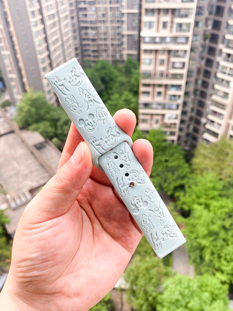 May include: A light blue silicone watch strap with a repeating pattern of embossed cartoon characters. The strap is designed for a smartwatch.